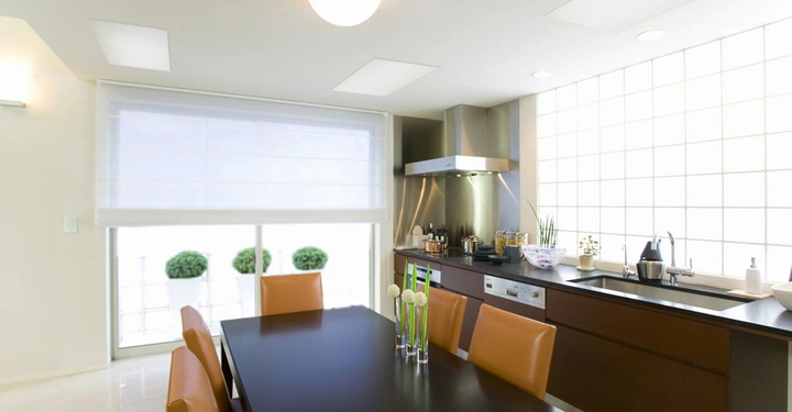 Galerie-Bild 8: Schwarzer Esstisch mit braunen Stühlen steht in einer modernen Küche mit Edelstahlgeräten und großen Fensterflächen; draußen sind grüne Büsche sichtbar.