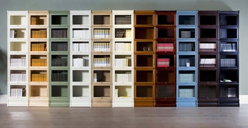 Regaleinheit mit mehreren Regalen in Reihen angeordnet enthält eine Vielzahl von Büchern. Verschiedene Farbtöne von Weiß über Beige zu Dunkelbraun. Steht in einem Raum mit Holzboden und grüner Wand.