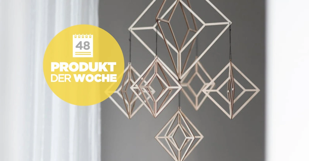 Geometrische Holzornamente hängen in einem Zimmer vor grauem Hintergrund. Gelber Kreis mit Text 48 PRODUKT DER WOCHE ist links im Bild.