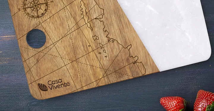 Holzschneidebrett mit Kompassrose und Weltkarten-Gravur, liegt auf dunklem Holzuntergrund, rechts einige Erdbeeren. Text: Casa Vivente.