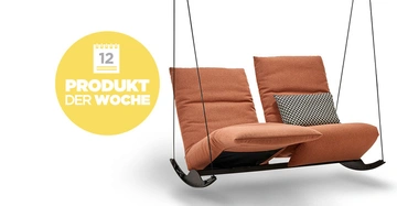 Zweisitzige Schaukel mit orangefarbenen Polstern und einem schwarz-weiß-gemusterten Kissen hängt an Seilen. Links gelbes Symbol mit Kalender und Text 12 PRODUKT DER WOCHE auf weißem Hintergrund