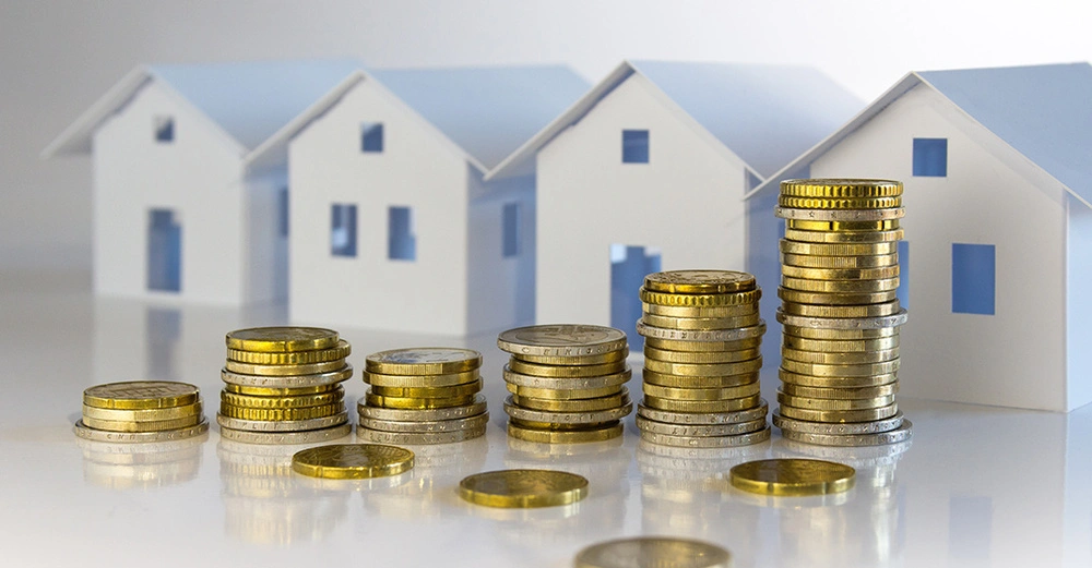 Gestapelte Euromünzen vor stilisierten Papierhäusern symbolisieren Immobilienpreise und Baufinanzierung.