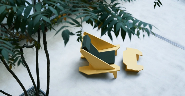 Moderne gelbe Stühle und ein Tisch stehen ohne Personen auf einer Steinoberfläche draußen umgeben von Bäumen und Blättern die von oben ins Bild ragen