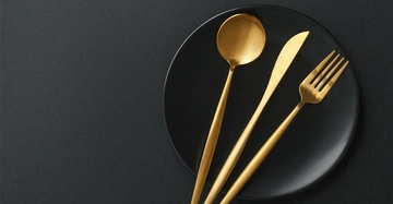 goldenes Besteckset aus Messer, Gabel und Löffel auf schwarzem Hintergrund