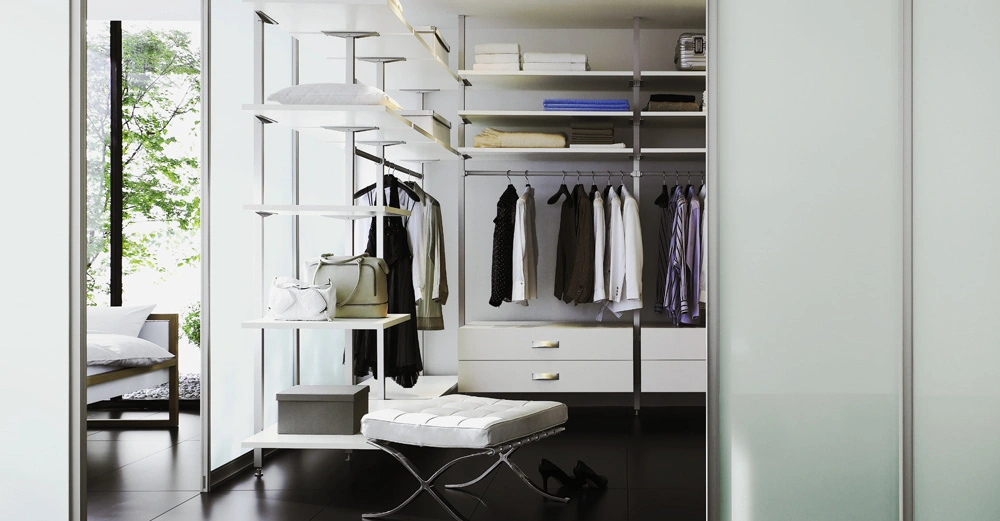 Eleganter und organisierter Kleiderschrank mit Regalen und hängender Kleidung über Schubladen im Kontext eines modernen begehbaren Kleiderschranks mit raumhohen Glaswänden und Blick auf ein grünes Außengelände.