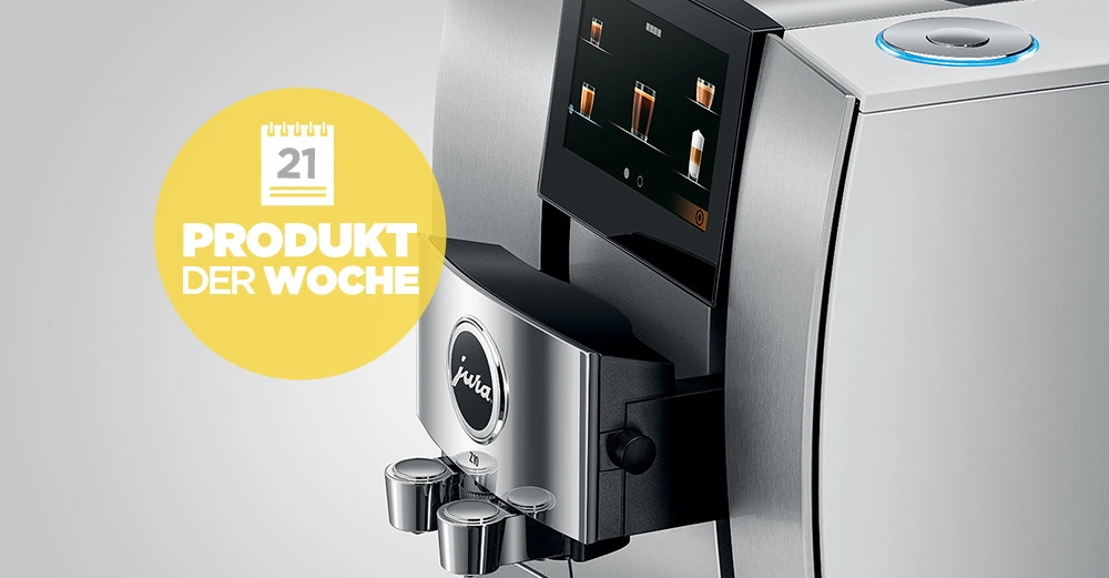 Eine silberne Kaffeemaschine der Marke Jura mit einem Display, die Kaffee zubereitet, steht auf einer grauen Oberfläche. Text auf gelbem Kreis 21 PRODUKT DER WOCHE