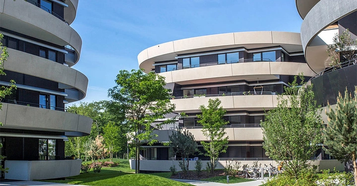 Moderne runde Mehrfamilienhäuser stehen still in einem grünen Garten mit Bäumen und Büschen im Vordergrund in einem Wohngebiet.