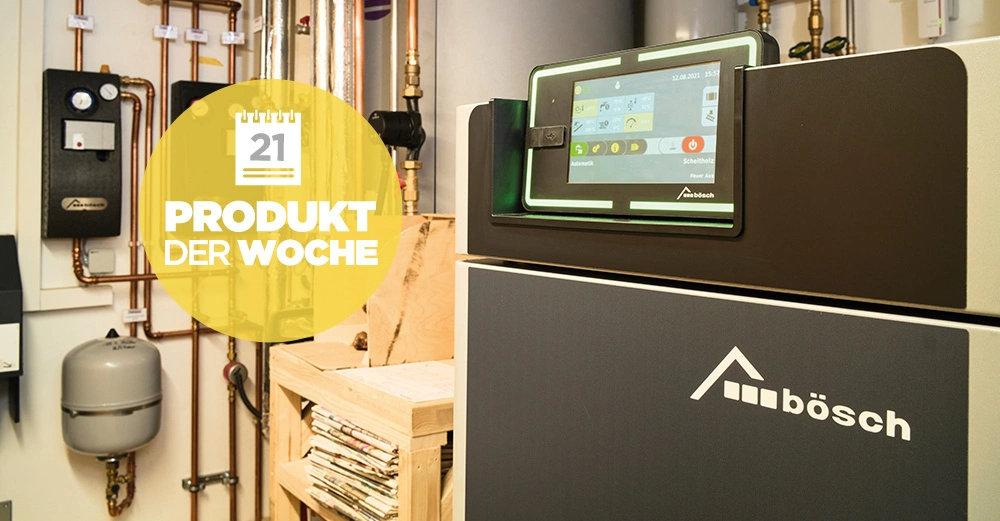 Heizkessel mit digitalem Display in Betrieb umgeben von Rohren und Heizungszubehör in einem Heizungsraum. Auf gelbem Hintergrund Text: 21 PRODUKT DER WOCHE
