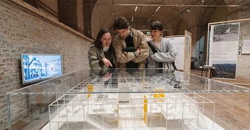 2 Frauen und ein Mann betrachten ein großes Architekturmodell auf einem Tisch im Architekturzentrum in Wien.