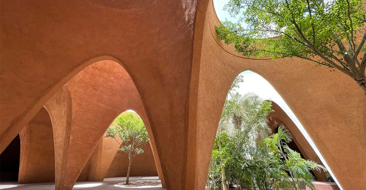 Galerie-Bild 3: Bäume stehen unter gebogenen, braunen Sandsteinbögen in einer offenen, architektonischen Struktur mit natürlichen Lichtdurchlässen, während im Hintergrund ein helles, sonniges Umfeld zu sehen ist.