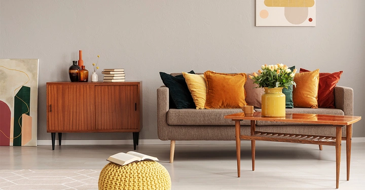 Ein Wohnzimmer mit einem braunen Sofa und einem hölzernen Beistelltisch. Auf dem Sofa liegen verschiedene Zierkissen in bunten Herbstfarben.