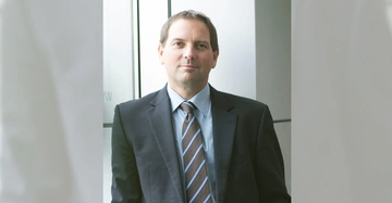 Mann trägt Anzug mit Krawatte steht gerade und blickt in die Kamera Umgebung ist ein moderner Bürogebäude-Hintergrund.