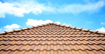 Dachziegel bilden ein gleichmäßiges Muster unter einem klaren blauen Himmel mit vereinzelten weißen Wolken.