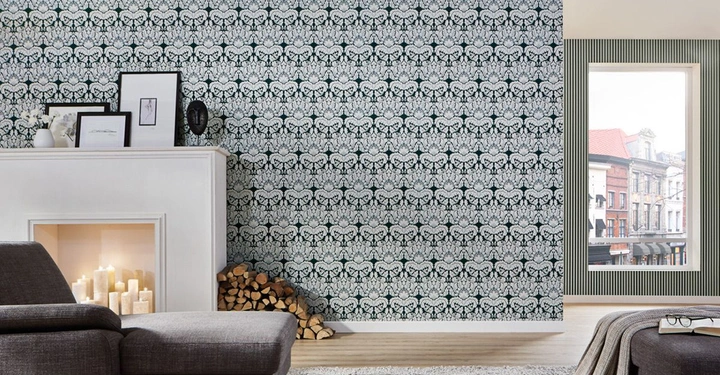 Ein graues Sofa steht vor einem dekorierten Kamin mit Kerzen daneben Holzscheite und Bilderrahmen an der Wand ist eine gemusterte Tapete ein offenes Fenster zeigt eine Straßenansicht