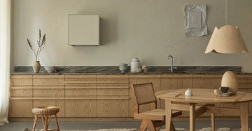 Küche mit Holzküchenschränken Vase und Töpfe auf Arbeitsplatte runder Holztisch mit Geschirr und Dekoobjekten Holzstuhl im Hintergrund Hängelampe und weißer Vorhang rechts und links