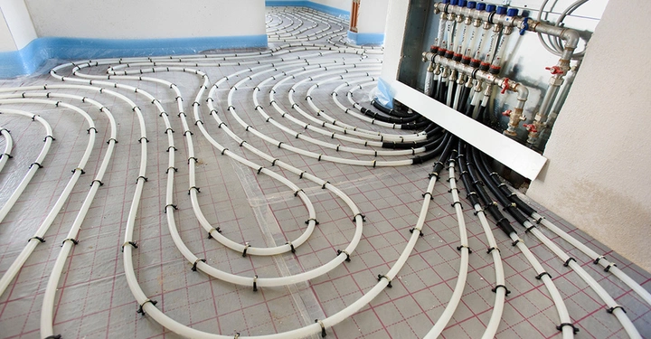 Installation einer Warmwasser-Fußbodenheizung in einem Neubau. Die weißen Heizungsrohre sind systematisch auf der Dämmung verlegt und führen zum Heizkreisverteiler, der in einer Wandnische montiert ist.