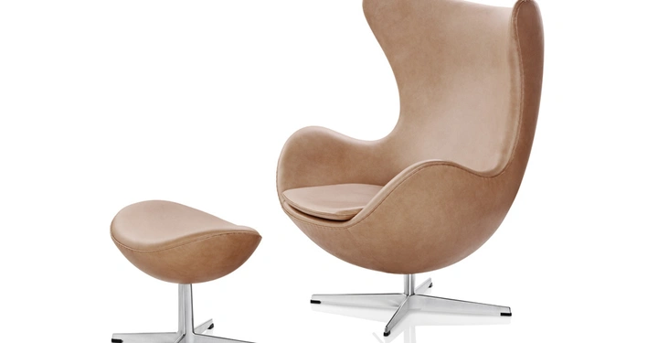 Galerie-Bild 4: Brauner Sessel in geschwungener Form stehend auf silbernem Fuß mit passendem Hocker beides auf weißem Hintergrund