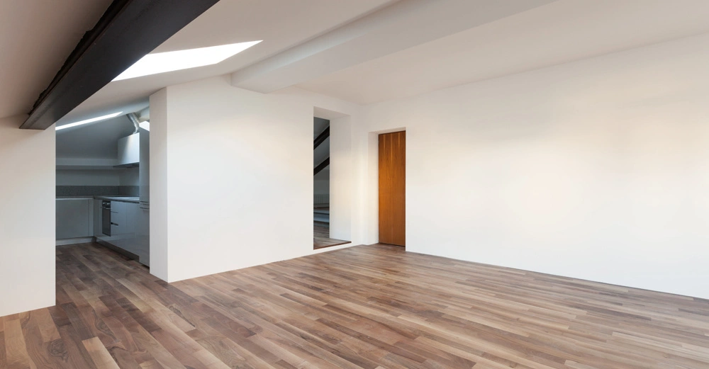 Leerer Raum Holzfußboden und weißen Wänden links eine offene Verbindung zur modernen Küche geradeaus eine Tür rechts ein großzügiger leerer Bereich Zimmer mit Balkendecken und Oberlichtern Wohnung Einrichtung.