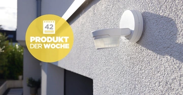 Bewegungsmelder in Weiß an grau verputzter Außenfassade, Anschnitt der Eingangstüre zu sehen. 