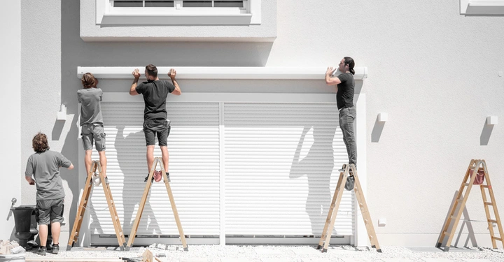 4 Monteure von hinten zu sehen, stehen auf Leitern und montieren den Kasten für eine große Markise an modernes Haus mit weißer Fassade