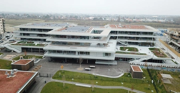 Großes modernes Gebäude mit mehreren Stockwerken Steht mitten in einer weitläufigen Umgebung Gebäude hat zahlreiche Balkone und flache Dächer Mit in der Ferne Wohngebäude und Vegetation.