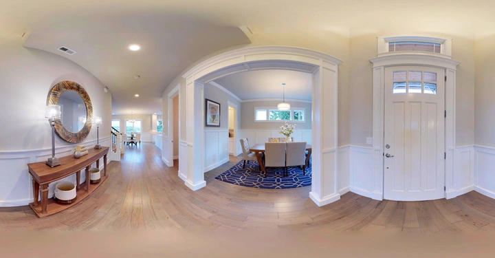 Eingangstüre öffnet sich zu einem Flur mit Holzboden und einer Konsole mit Spiegel links; daneben Esszimmer mit Teppich und Tisch; im Hintergrund offene Küche.