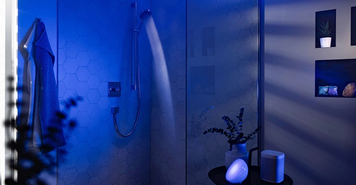 Dusche läuft Wasser blauer Lichteffekt moderner gefliester Duschbereich Handtuch hängt an der Wand Pflanzen und Dekor im Hintergrund durch Glastrennwand sichtbar Badezimmer Zubehör auf einem Tisch