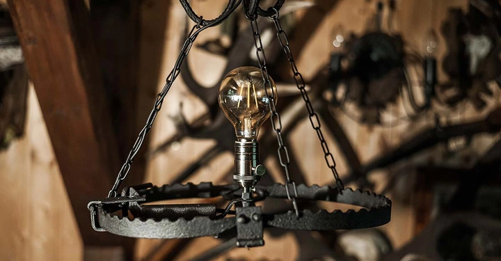 Glühbirne hängt an Ketten von einer Metallfalle in einem rustikal eingerichteten Raum.