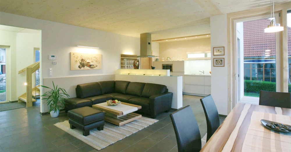 Ecksofa - steht in einem modernen Wohnzimmer mit einem Teppich und Couchtisch, angrenzend an ein Esszimmer und eine offene Küche, daneben Pflanzen und gerahmte Bilder an der Wand.