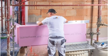 Bauarbeiter mit Austrotherm T-Shirt dämmt Sockel eines Rohbaus mit rosafarbenen Dämmstoffplatten.