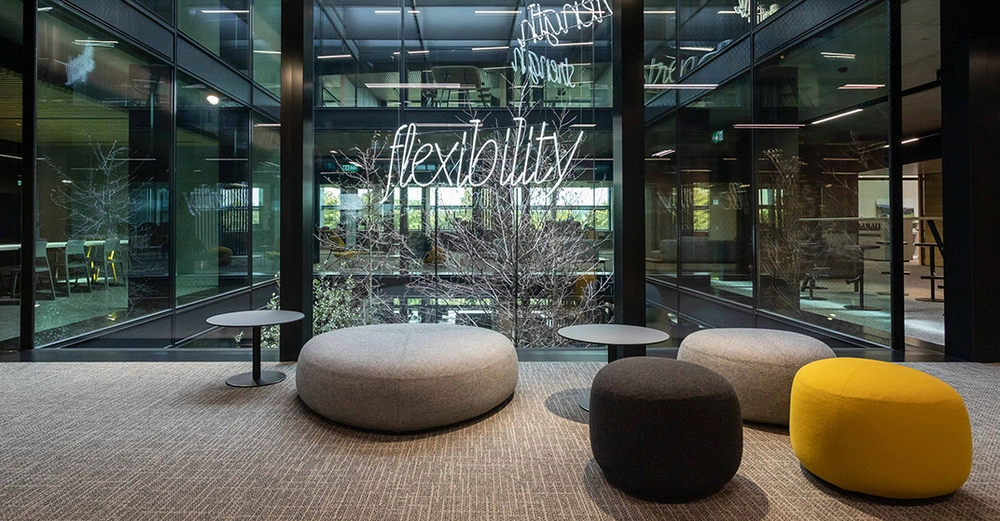 Sitzbereich mit verschieden großen Puffs in Grau und Gelb im Büro der HABAU GROUP in Linz, im Hintergrund der begrünte Innenhof