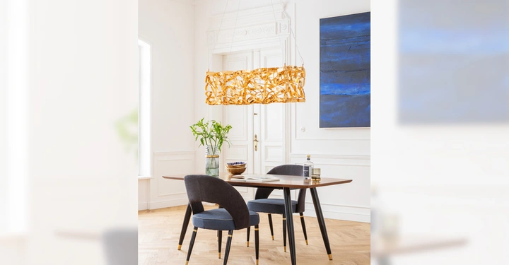 Galerie-Bild 1: Tisch steht im Vordergrund zwei Stühle und eine Glasvase mit Pflanzen darauf großes abstraktes blaues Gemälde an der Wand im Hintergrund Lampe mit goldenem Schirm über dem Tisch helle Umgebung