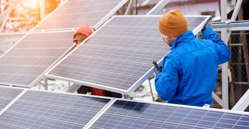 Zwei Arbeiter montieren Solarpaneele im Freien bei Sonnenuntergang während des Winters in einer verschneiten Umgebung
