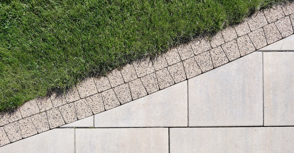 saftig grüner Rasenstreifen neben schmalem Pflaster neben großen Wegplatten. Ein Dreigestirn aus Vogelperspektive