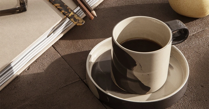 Galerie-Bild 1: Braunbeige Kaffeetasse mit Untertasse von fermLIVING steht auf Steintisch neben einem Tablet, Abendstimmung mit Sonne 