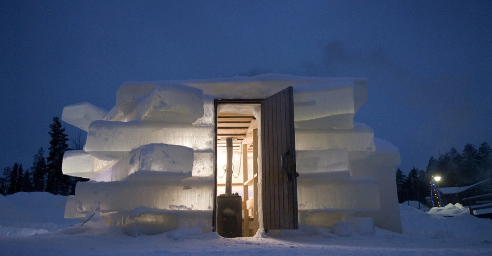 Eine Holztür führt in eine aus Eisblöcken gebaute Hütte im verschneiten Winterwald bei Dämmerung.