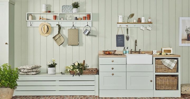 Helle Küche mit pastellgrünen Schränken wäscht Geschirr Waschbecken geben Gemütliche Atmosphäre Rechts Schreibtafel mit Text Die Besten Tage Beginnen mit einem Lächeln Links saubere Arbeitsfläche Pflanzen Accessoires und Dekorationen überall