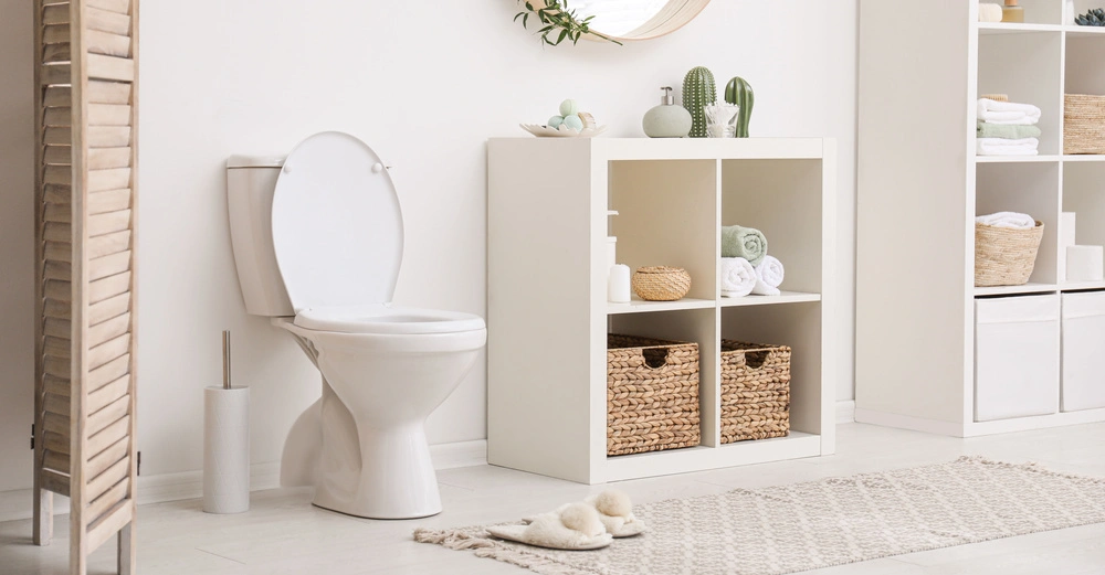 Toilette in einem modernen Badezimmer steht neben einem weißen Regal mit Körben und Handtüchern auf einem hellen Teppich in einem sauberen und hellen Raum