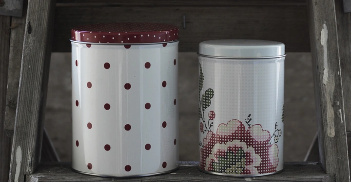 Galerie-Bild 6: Zwei verzierte Blechdosen stehen auf einer alten Holzleiter die linke Dose hat rote Punkte die rechte Dose hat ein florales Muster. Im Hintergrund ist eine unscharfe Wand zu sehen.