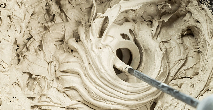 Flexibler Fliesenkleber wird mit einem Rührquirl im Eimer professionell angemischt. Die cremige Konsistenz des Klebermörtels ist entscheidend für die Haftung der Fliesen.