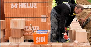 Bauarbeiter verarbeitet HELUZ SIDI Dünnbettmörtel beim Errichten einer Ziegelwand aus HELUZ-Ziegeln auf einer Baustelle.