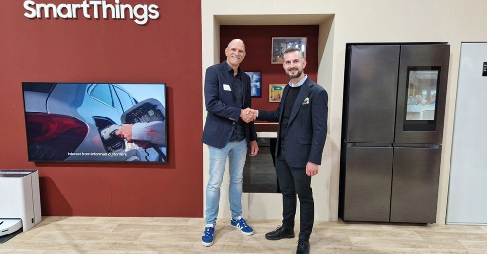 Thorsten Boecker von Samsung und Simon Becker von Home One schütteln sich in einen rot gestrichenen Schauraum mit Smart TV die Hände.