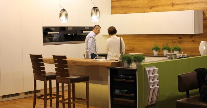 Galerie-Bild 15: Zwei Personen stehen in einer modernen Küche und betrachten etwas auf der Arbeitsplatte Die Küche hat helle Schränke Holzwände und zwei Hocker vor einer Frühstückstheke Die Umgebung wirkt einladend und wohnlich