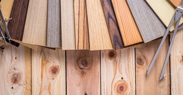 Holzmuster in verschiedenen Farben liegen ausgebreitet auf einer Holzfläche zusammen mit einem aufgeklappten Zirkel.