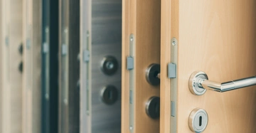 Türgriff an einer Holztür teilweise geöffnet im Vordergrund sichtbar im Hintergrund mehrere gesicherte Türen in verschiedenen Farben ausgestellt in einer Reihenaufnahme