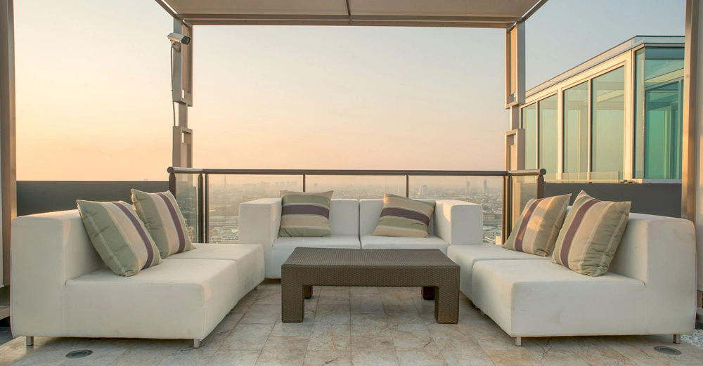 Weiße Sofas mit gestreiften Kissen stehen um einen niedrigen Couchtisch auf einer Terrasse mit Dach in einem Hochhaus mit Stadtblick bei Sonnenuntergang