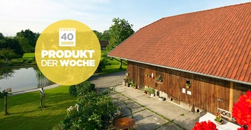 Ein großes Bauernhaus mit rotem Dach steht neben einem Teich in einer grünen Landschaft viele Pflanzen und Blumen in Töpfen stehen herum Text auf gelbem Kreis 40 PRODUKT DER WOCHE
