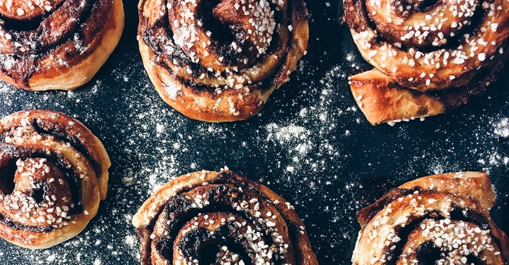 Zimtschnecken liegen auf einer dunklen Oberfläche verstreut mit Mehl und Zucker bestreut