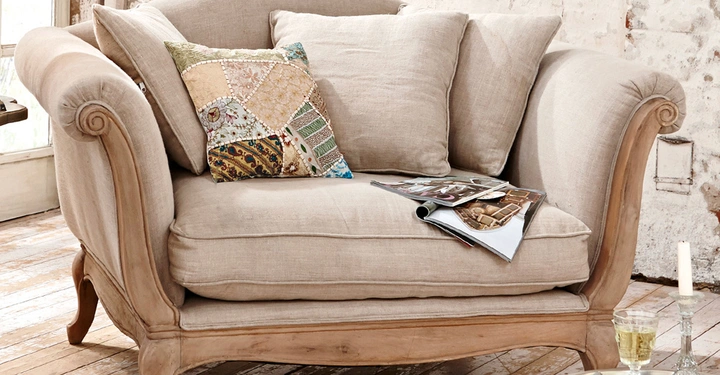 Galerie-Bild 1: Ein beiger Sessel mit zwei einfarbigen Kissen und einem Patchwork-Kissen darauf. Ein aufgeschlagenes Magazin liegt auf dem Sessel. Im Hintergrund sind helle Wände und ein Holzboden.