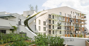 Mehrstöckiges modernes Gebäude kaskadenartige Dachbegrünung vorne Pflanzen auf der Terrasse im Hintergrund blauer Himmel mit Wolken städtische Umgebung Wohnungen mit Balkonen entlang der Fassade